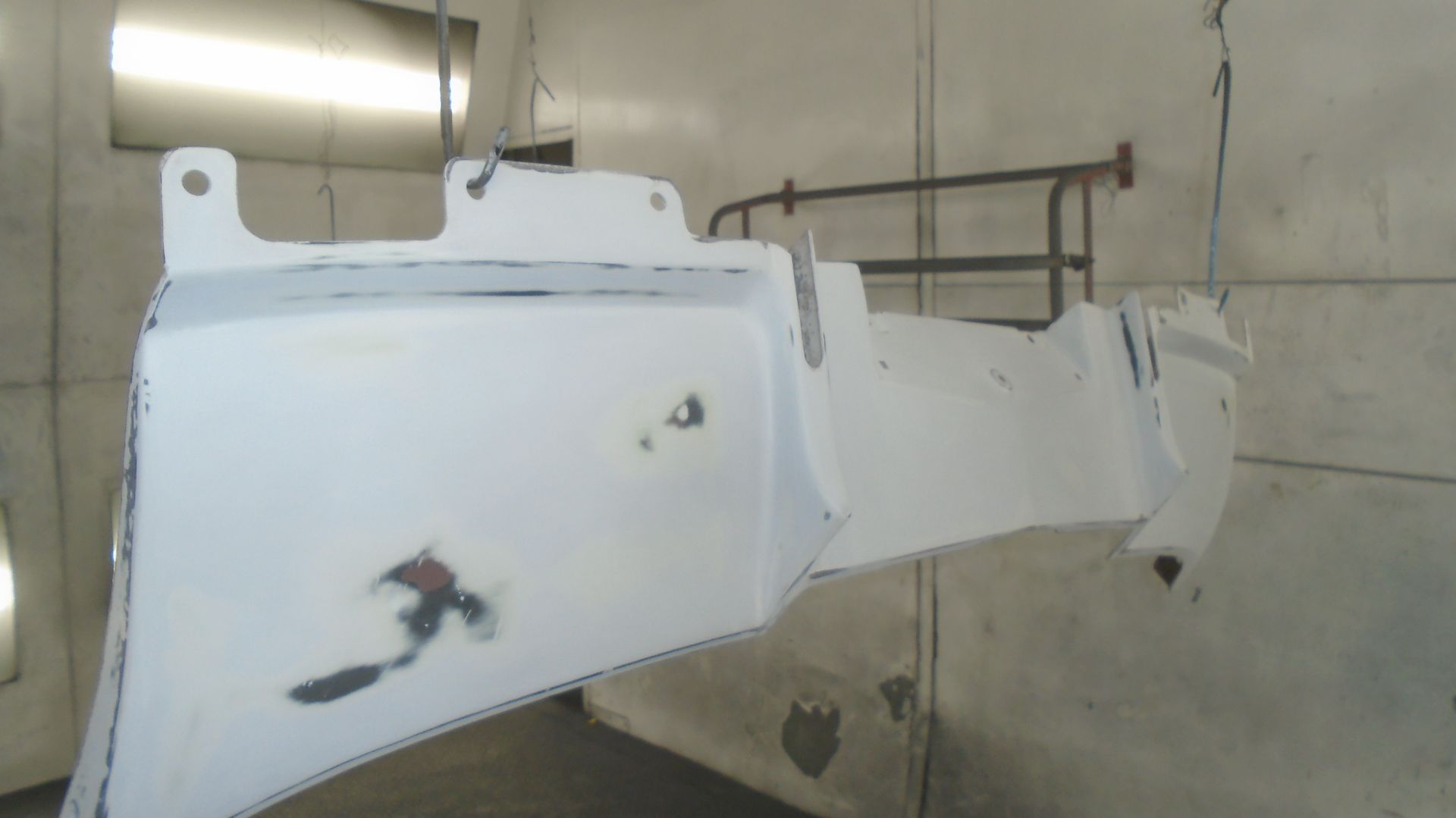 White vehicle bumper in a spray paint booth, showing repairs and preparation.