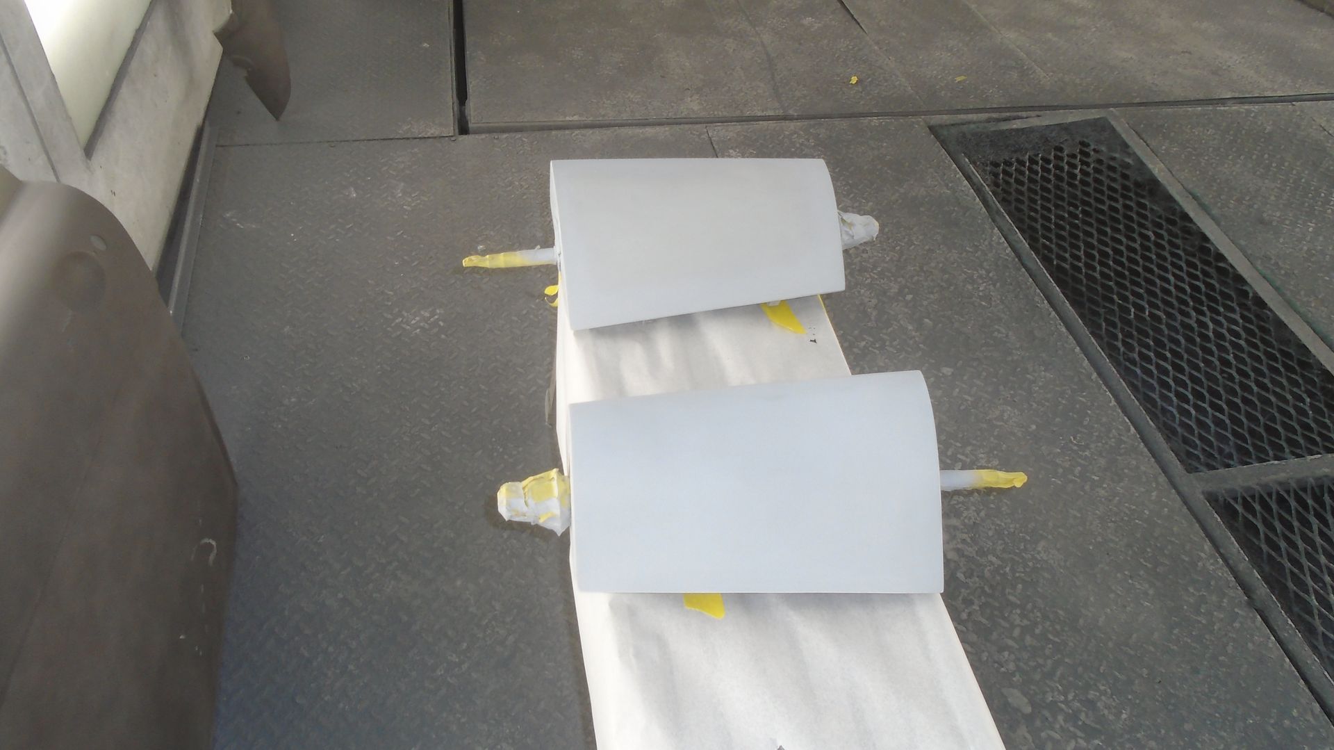 Two gray painted car panels resting on tape in a spray booth.