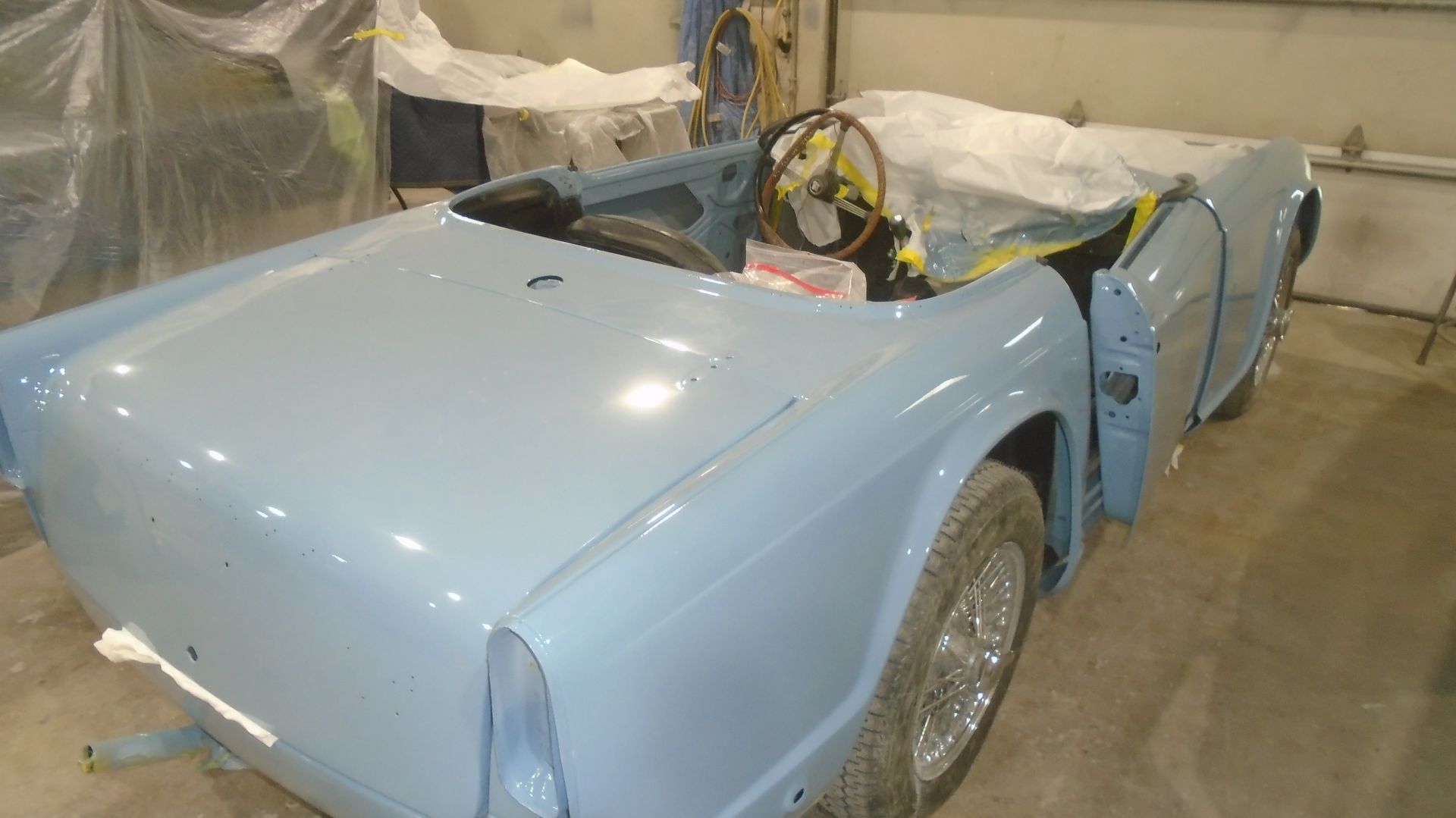 Light blue classic convertible car in a garage, under construction.