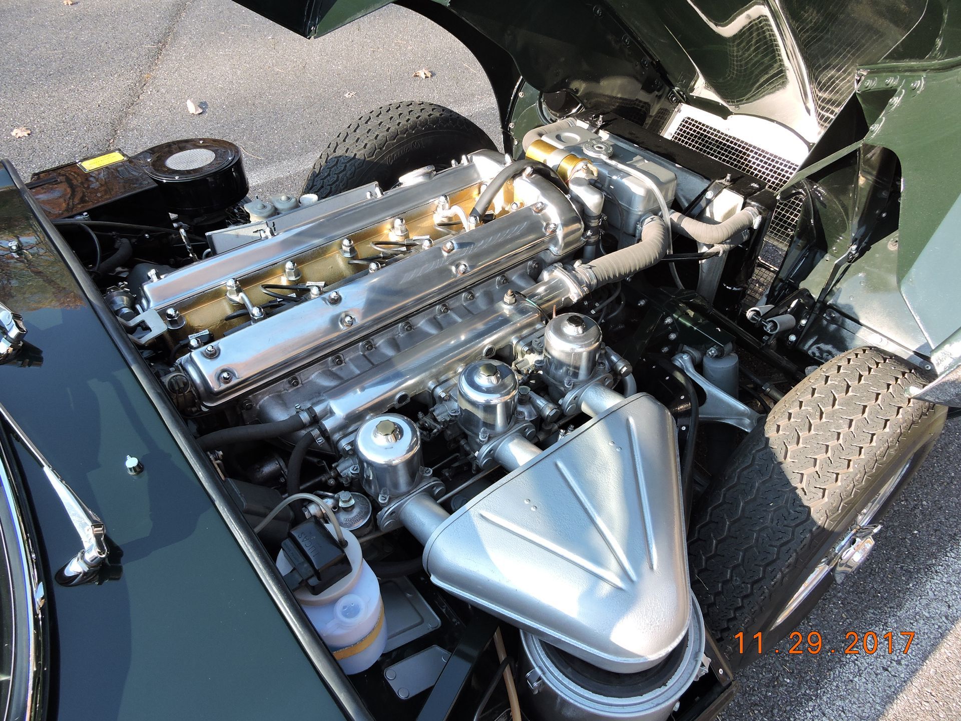 Green Jaguar E-type engine bay, detailed view of the engine, polished metal and chrome, outdoors.