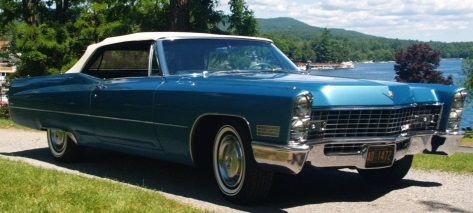 Blue convertible Cadillac on a road, with white top, near a lake.