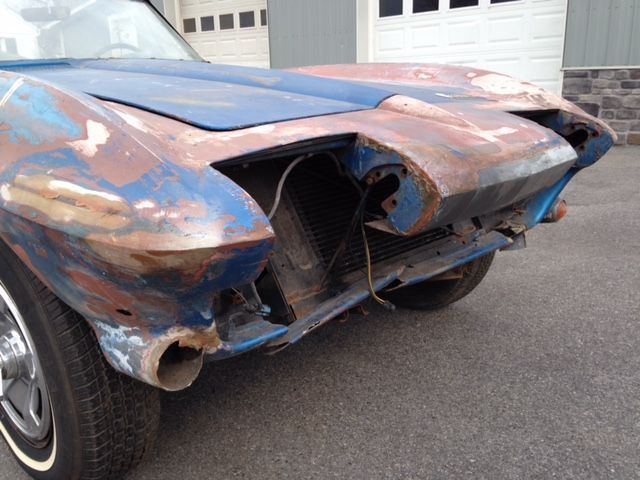 Heavily rusted blue classic car, front end damaged, in front of a white garage.