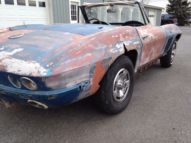 Classic, weathered blue and red convertible Corvette on asphalt, showing signs of wear and tear.