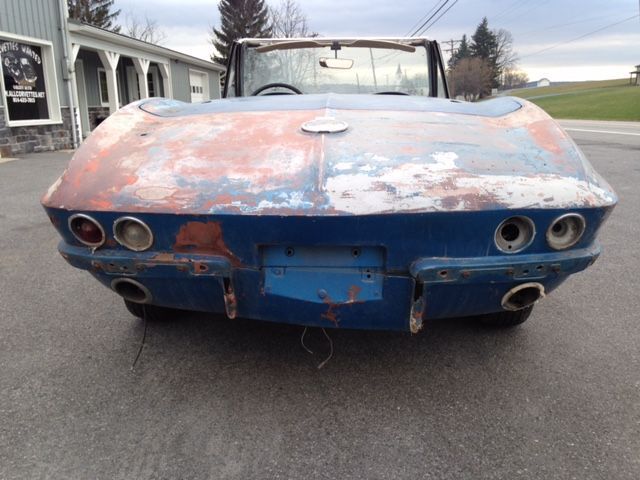Rear view of a weathered blue classic Corvette convertible with visible rust and missing parts.