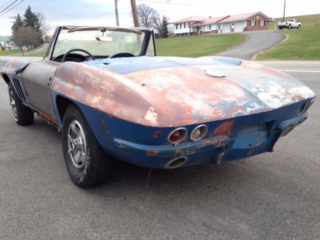 Rusty blue and brown convertible car, likely vintage, parked by a road.