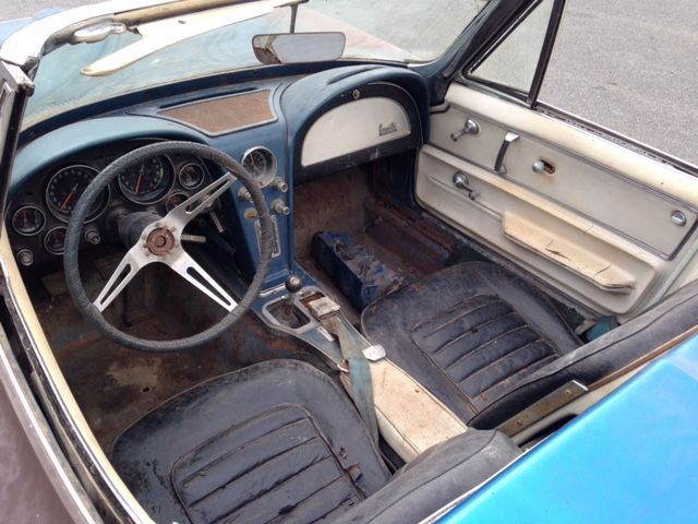 Interior of a vintage blue Corvette convertible, showing worn seats, dashboard, and steering wheel.