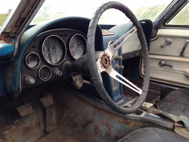 Interior of a classic blue car with a weathered dashboard, steering wheel, and gauges.