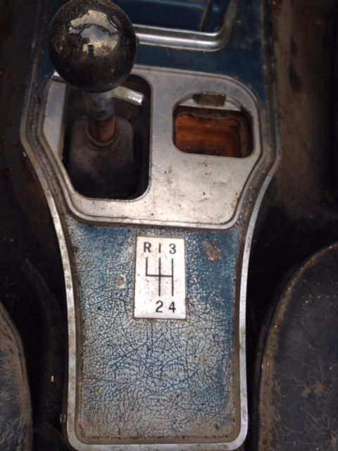 Close-up of a car's gear shift console with a four-speed stick shift. White and blue console with numbers: R13 and 424.