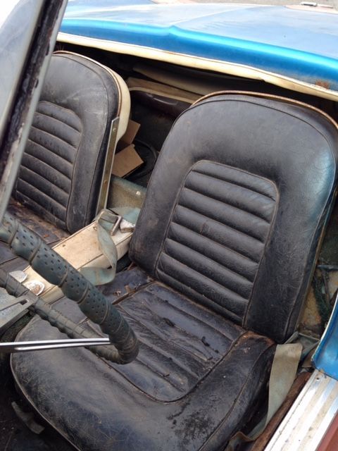 Black car seats with ribbed detail in a weathered, open-top blue classic car.