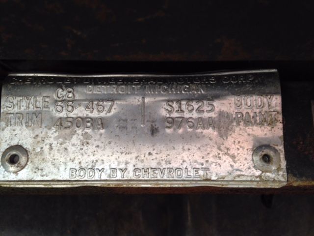 Silver vehicle identification plate with stamped codes, mounted on a dark surface.