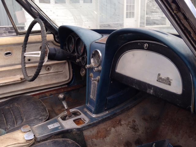 Interior of a weathered blue classic Corvette, showing gauges, steering wheel, and console.