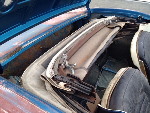 Blue convertible top folded down in the car's trunk, beige fabric, metal frame, rusty interior.