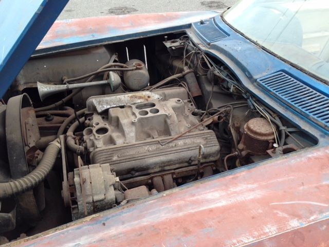 Rusty engine compartment of an old blue car, with visible engine components and wires.