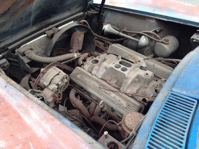 Open car hood revealing a dusty engine bay with an aged V8 engine and exhaust headers.