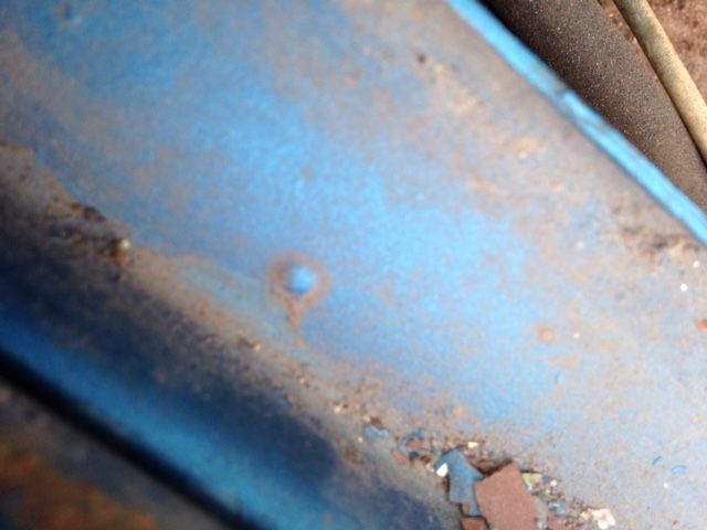 Close-up of weathered blue metal with rust and a small raised bump.