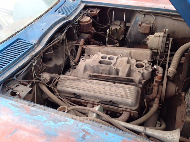 Blue classic car engine bay with a dusty V8 engine, and chrome Corvette valve covers.
