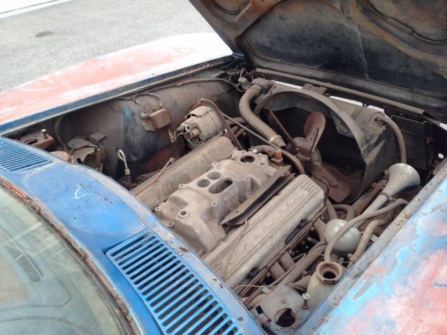 Rusty car engine with exposed parts under the hood. Blue and red paint, dusty setting.