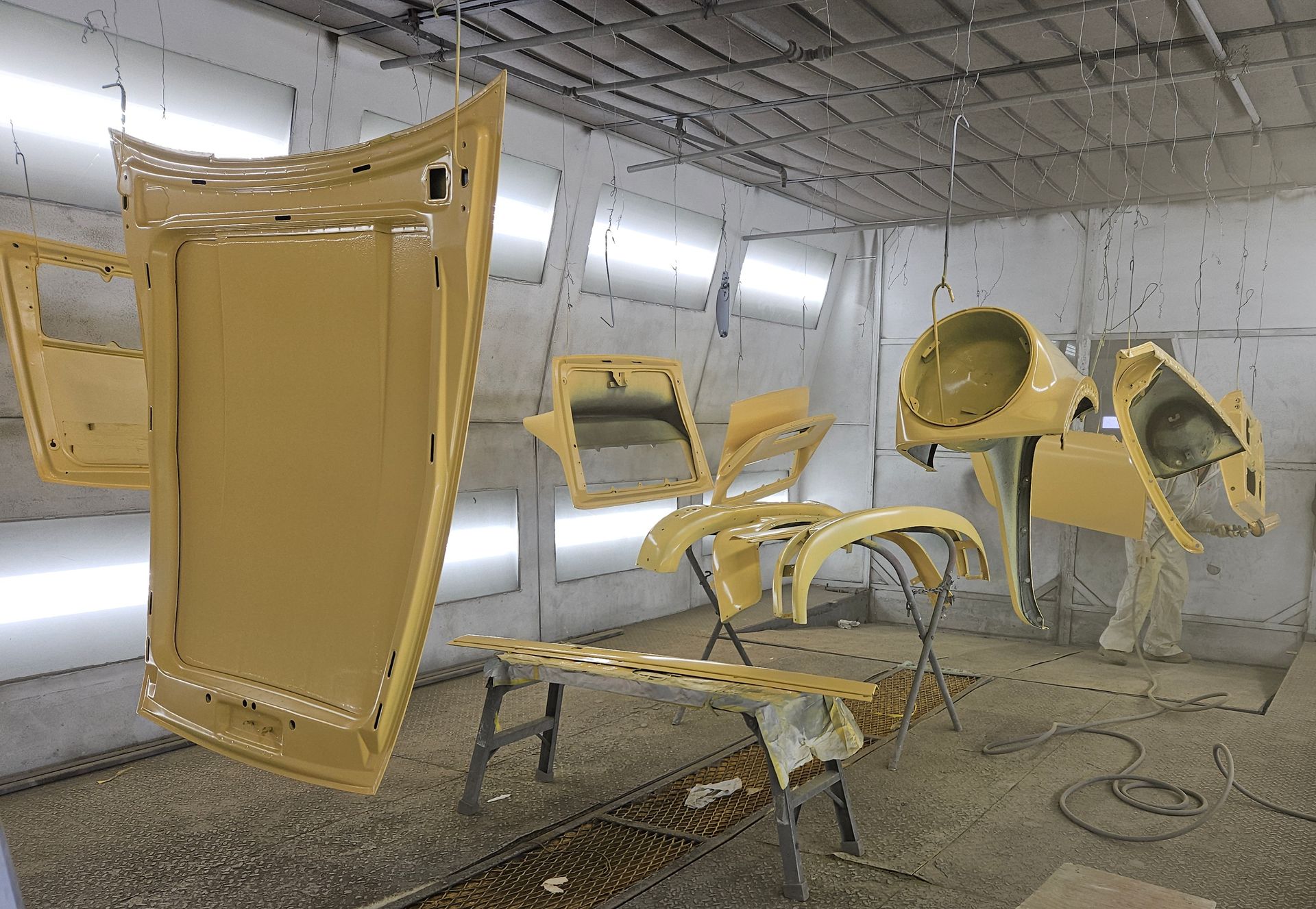 Car parts, painted yellow, hang in a paint booth.