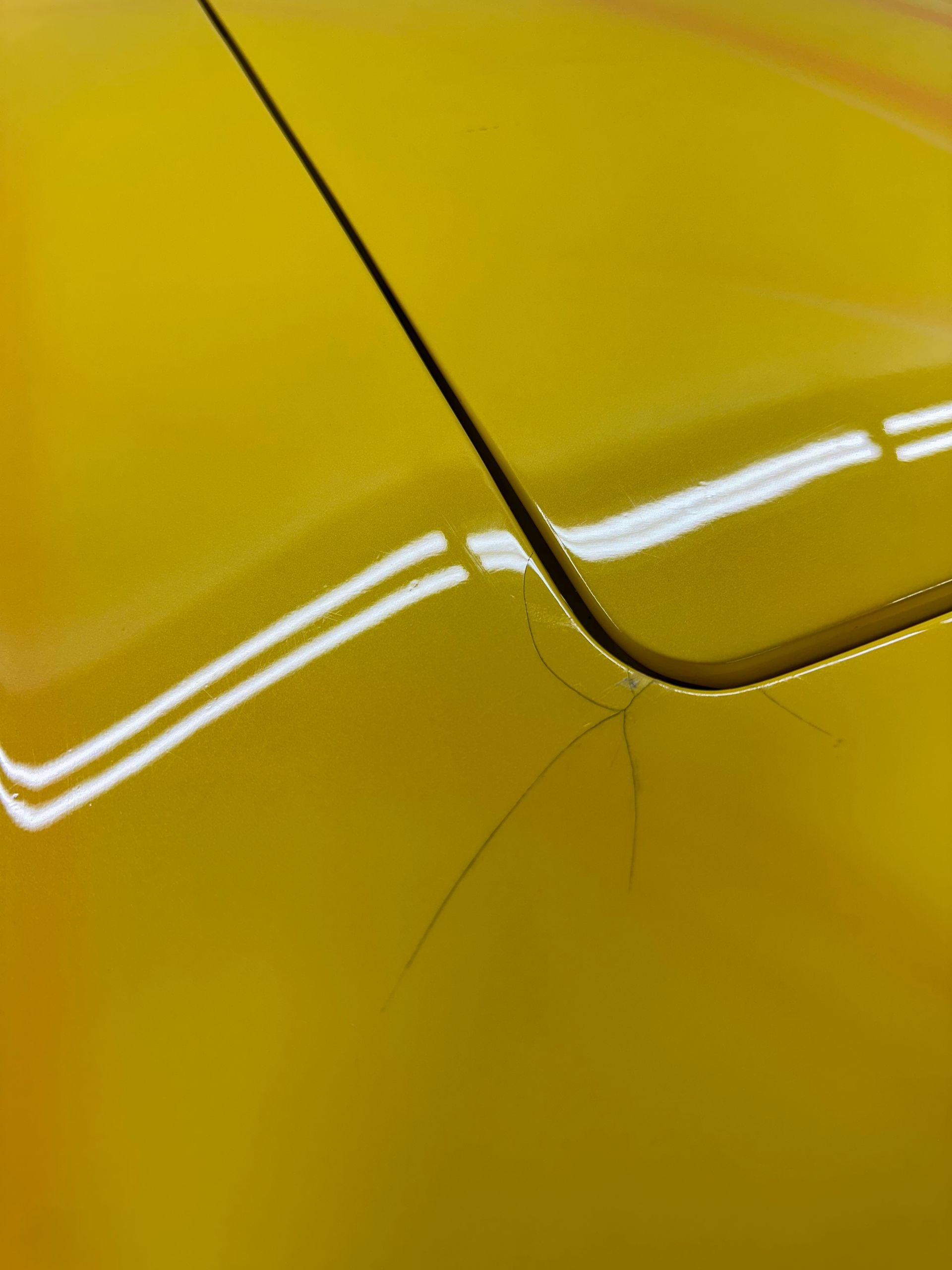 Yellow car paint with spiderweb-like cracks near a panel seam, reflecting light.