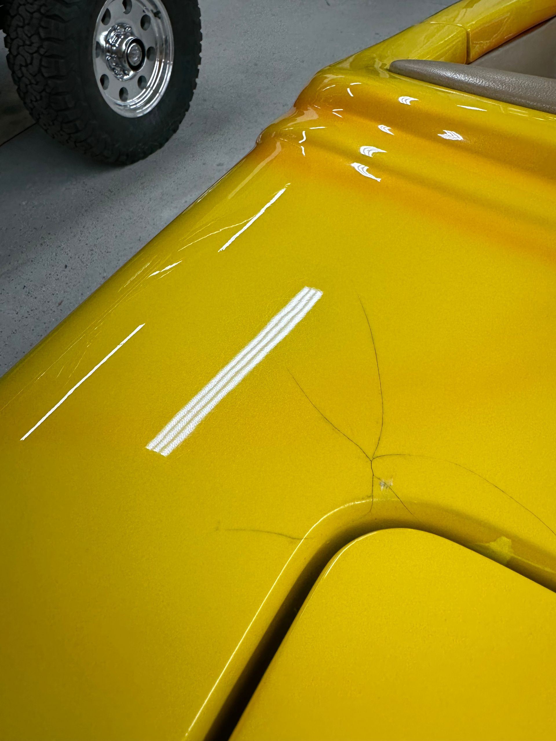 Yellow car part with visible cracks and a partial view of a tire.