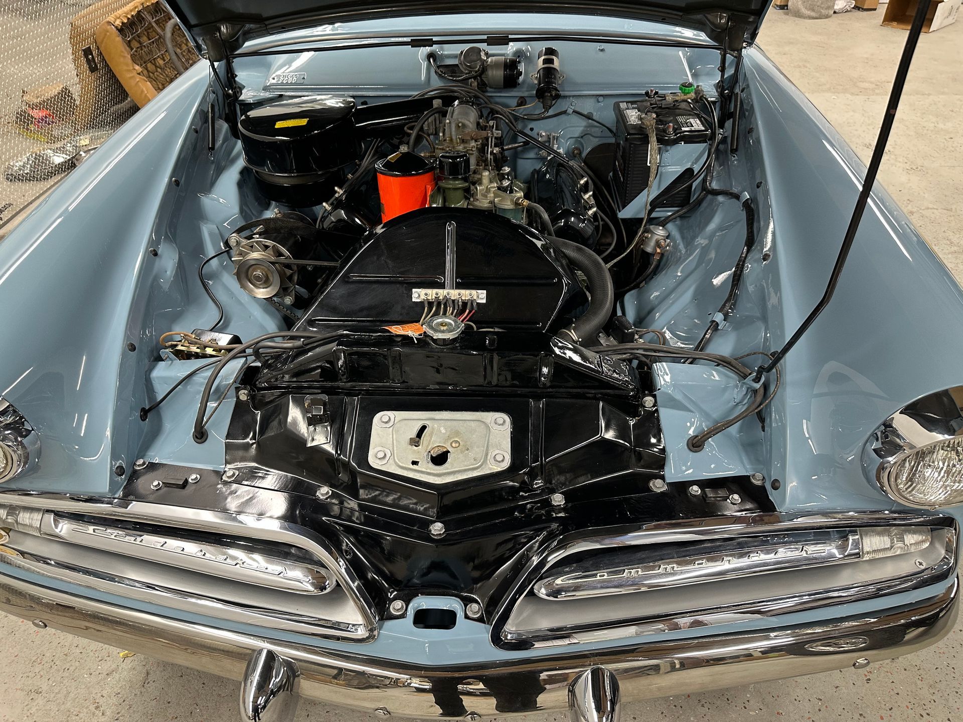 Light blue classic car engine bay, black engine components, chrome grill.
