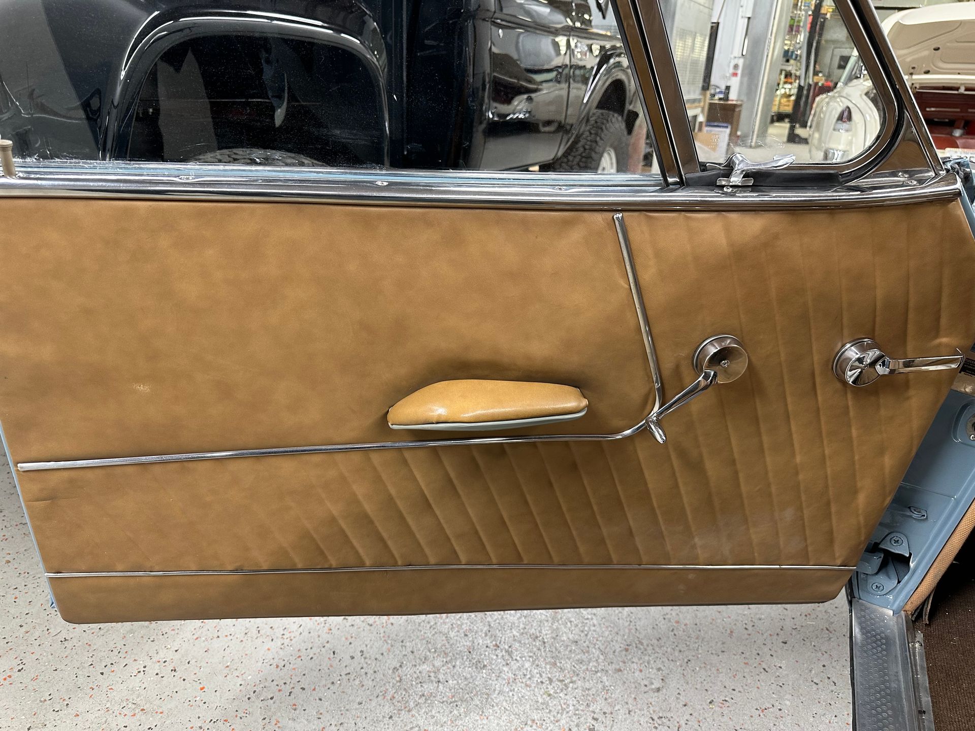 Tan car door panel with chrome trim, handle, and armrest.