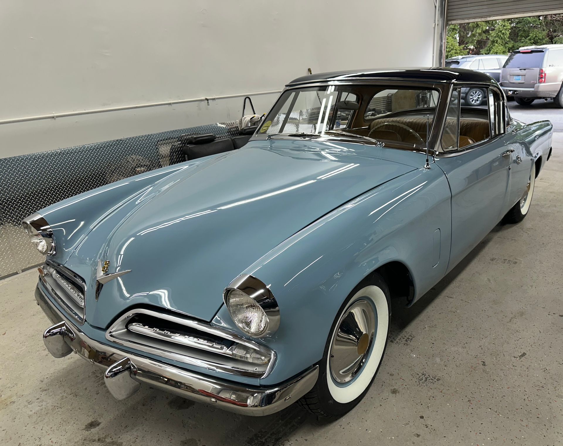 Blue and black vintage Studebaker coupe with white-walled tires parked inside a garage.