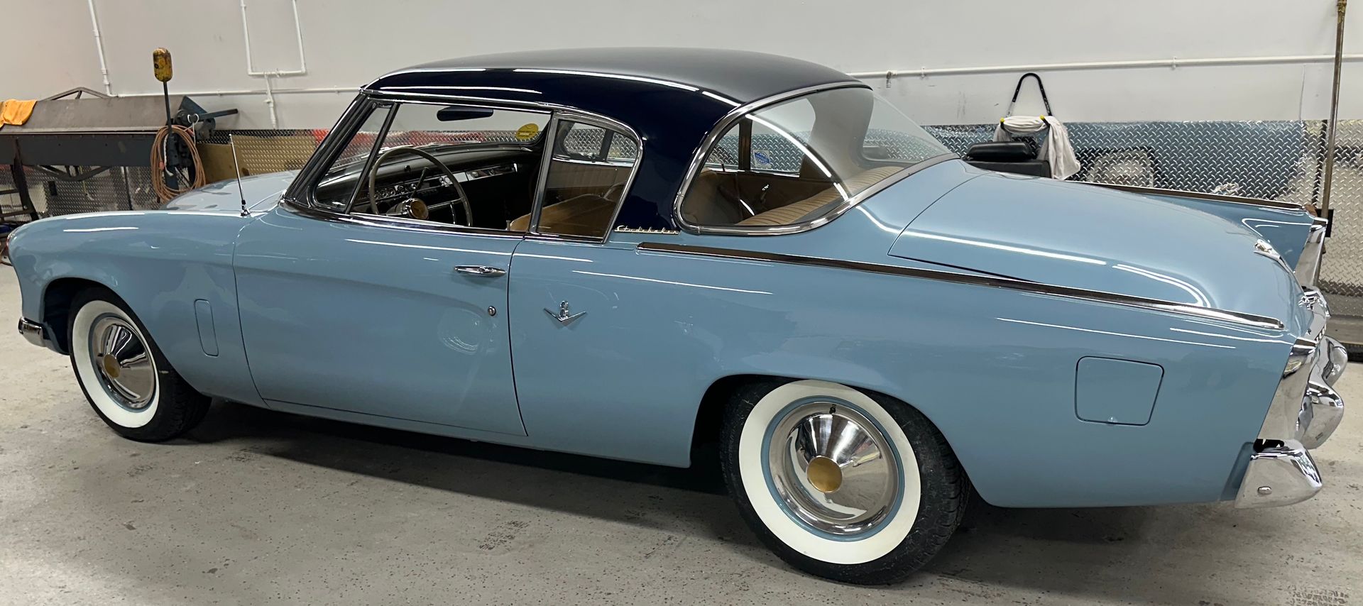Blue classic car with white-wall tires, and a dark blue roof. In a garage setting.
