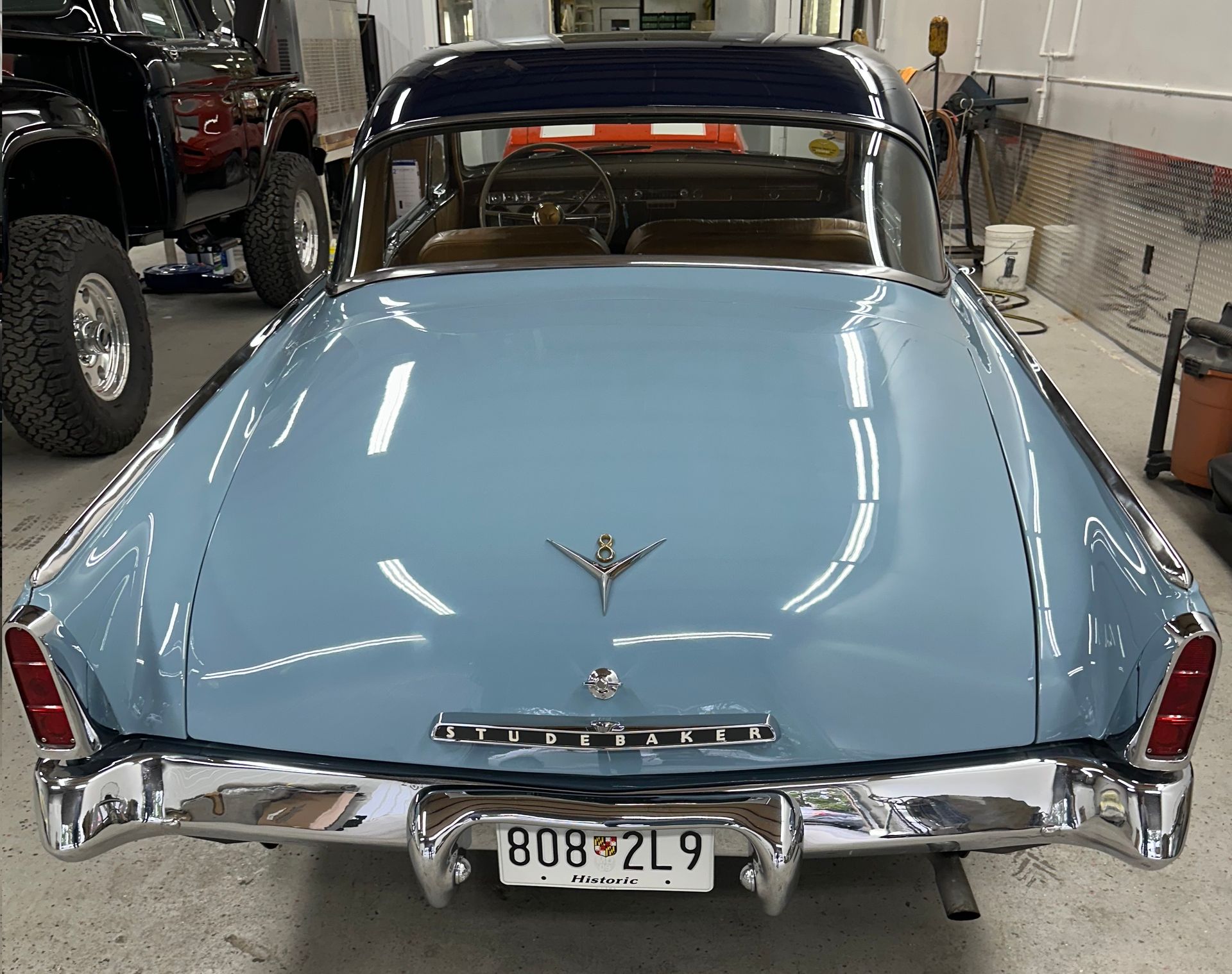 Rear view of a light blue and dark blue classic car with chrome accents, parked indoors.
