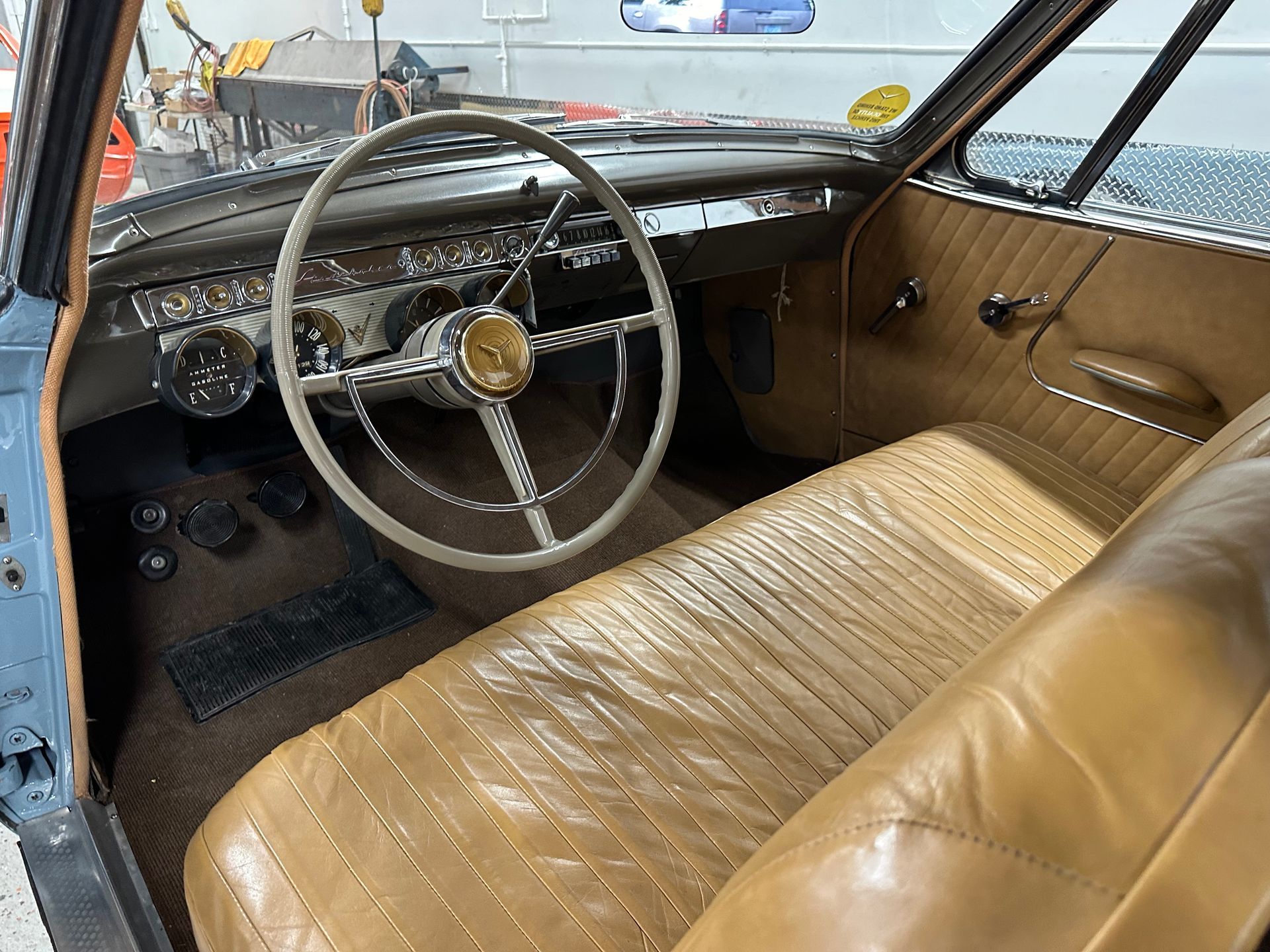 Interior of a vintage car with tan leather seats, light-colored steering wheel, and a dark dashboard.