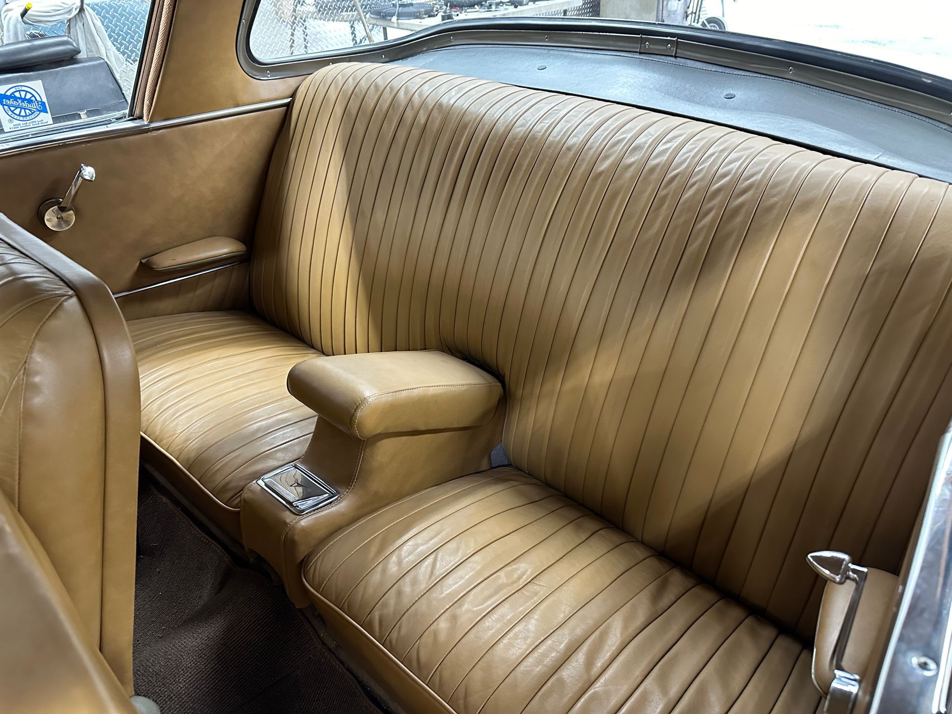 Tan leather car backseat with vertical stitching, armrests, and console.