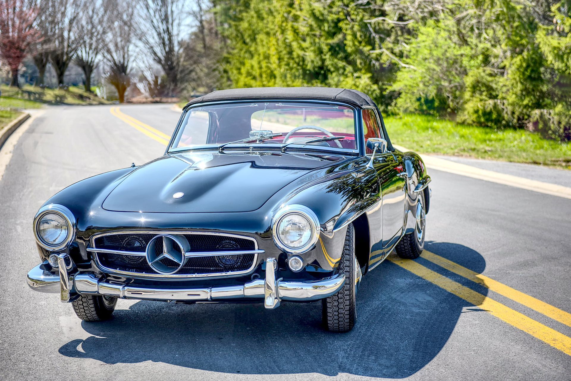 Black Mercedes-Benz 190SL convertible parked on a road with yellow lines, sunny day.
