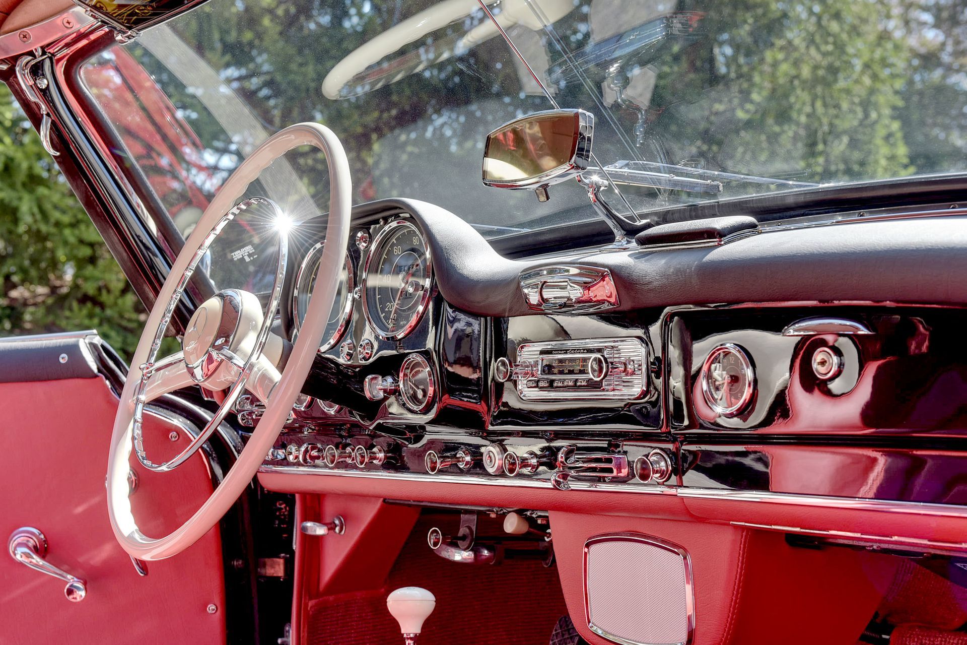 Interior of a vintage red convertible car with a white steering wheel and chrome dashboard details.