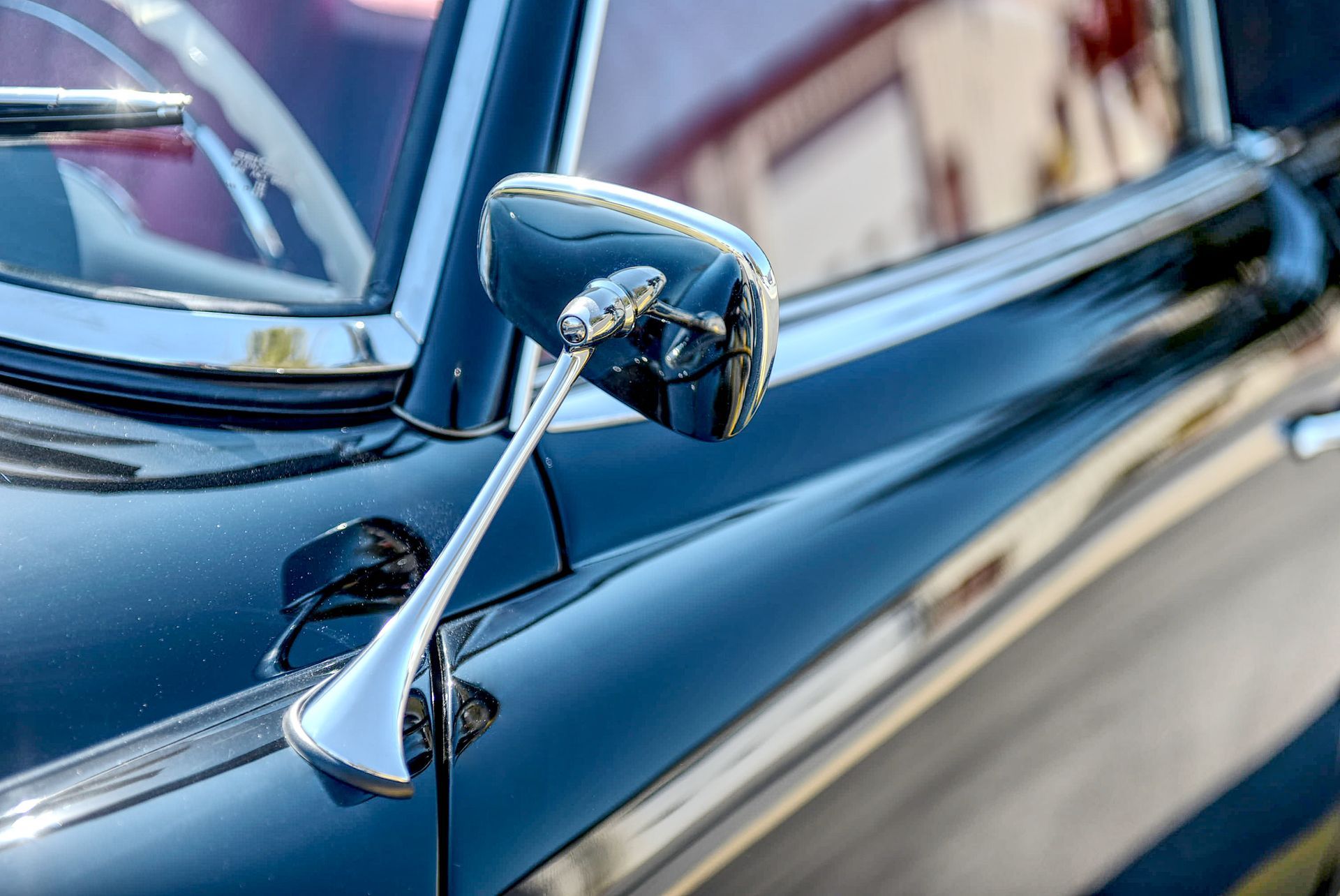 Chrome side mirror of a classic black car with white steering wheel visible.
