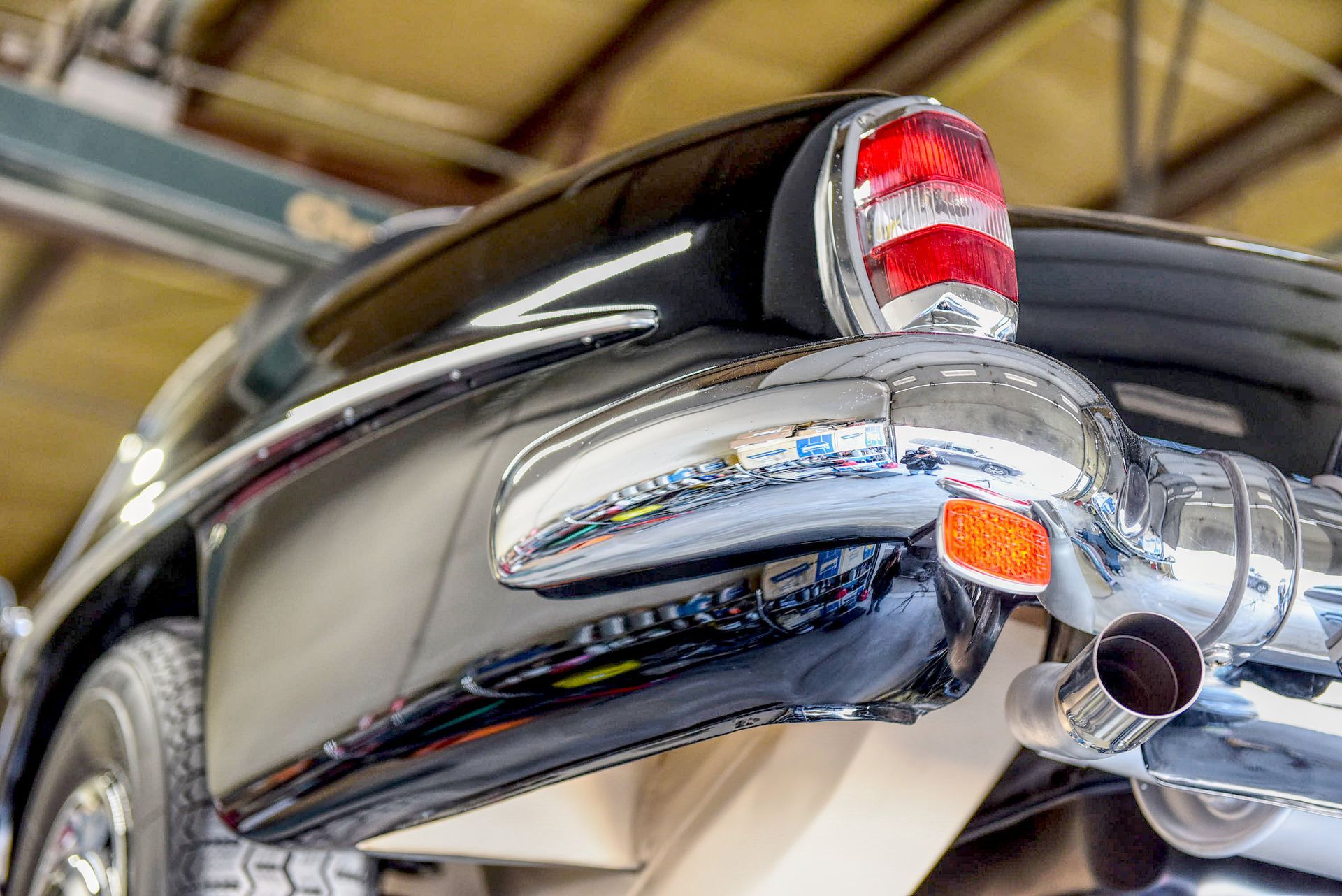 Black classic car's rear, chrome bumper, taillight, and exhaust pipes.