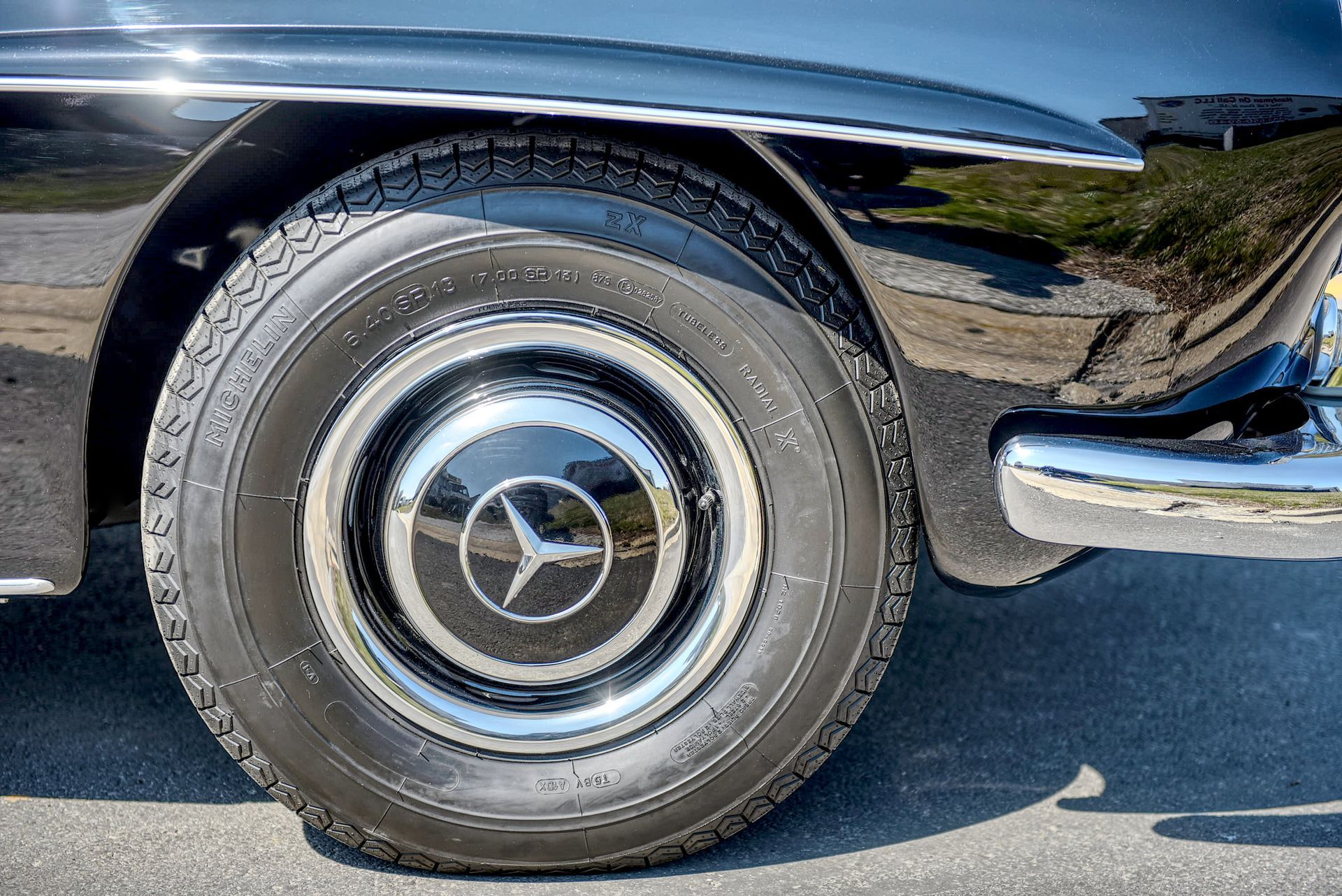Black classic Mercedes-Benz car tire and hubcap with a star logo, parked outdoors.