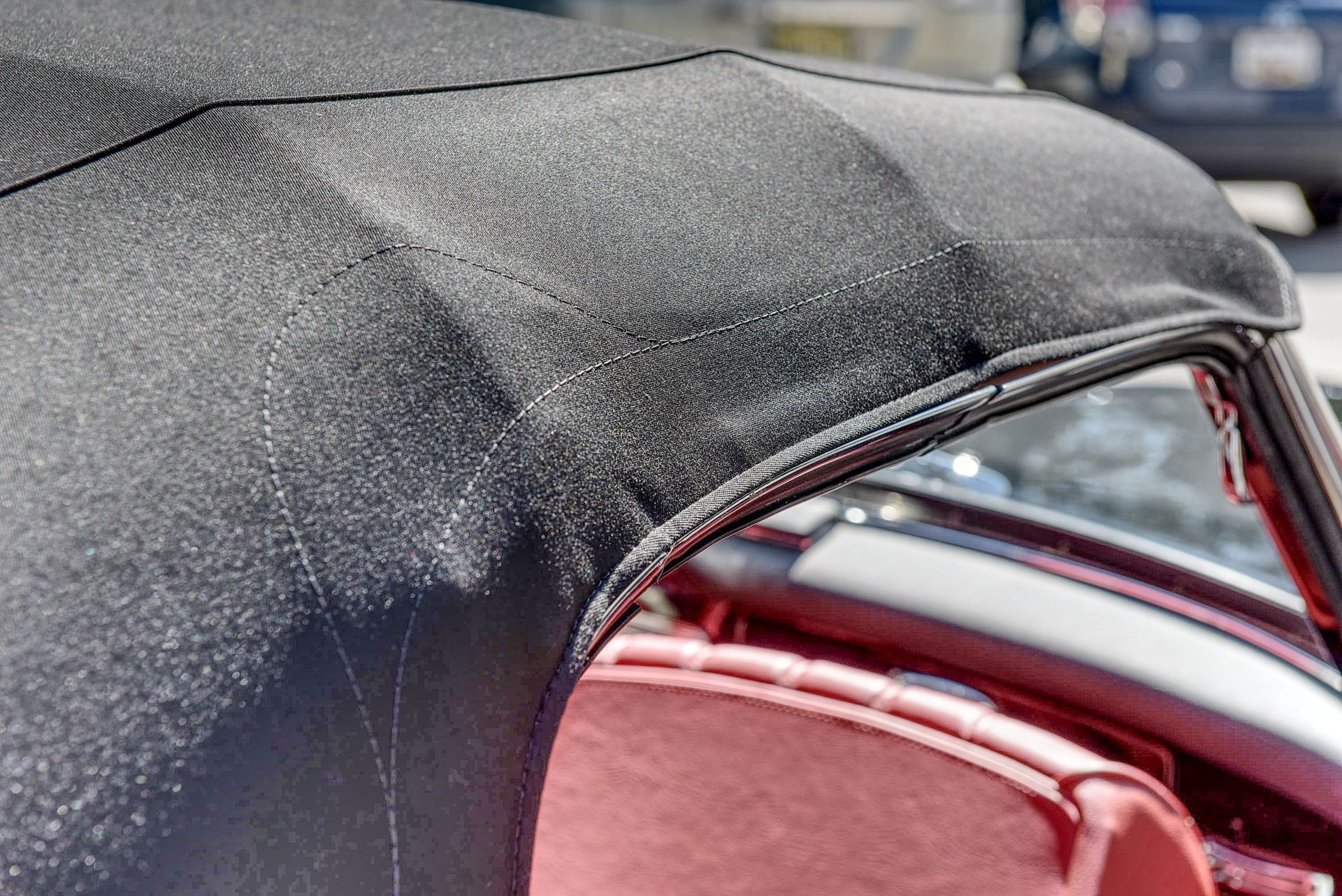 Black convertible top, stitched detail, frame visible, over red interior.