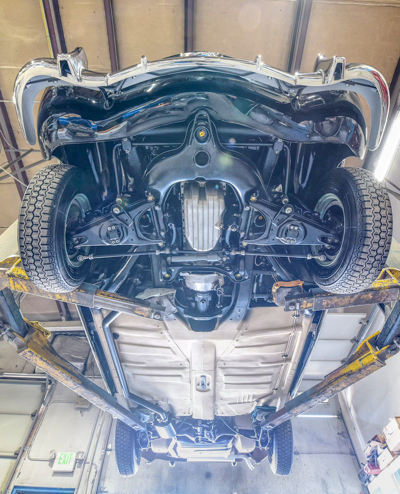 Underside of a black car on a lift in a garage, showing suspension and exhaust components.