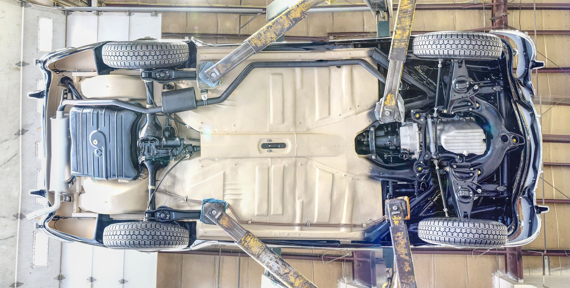 Underside view of a car on a lift in a garage. Shows the chassis, wheels, and mechanical components.