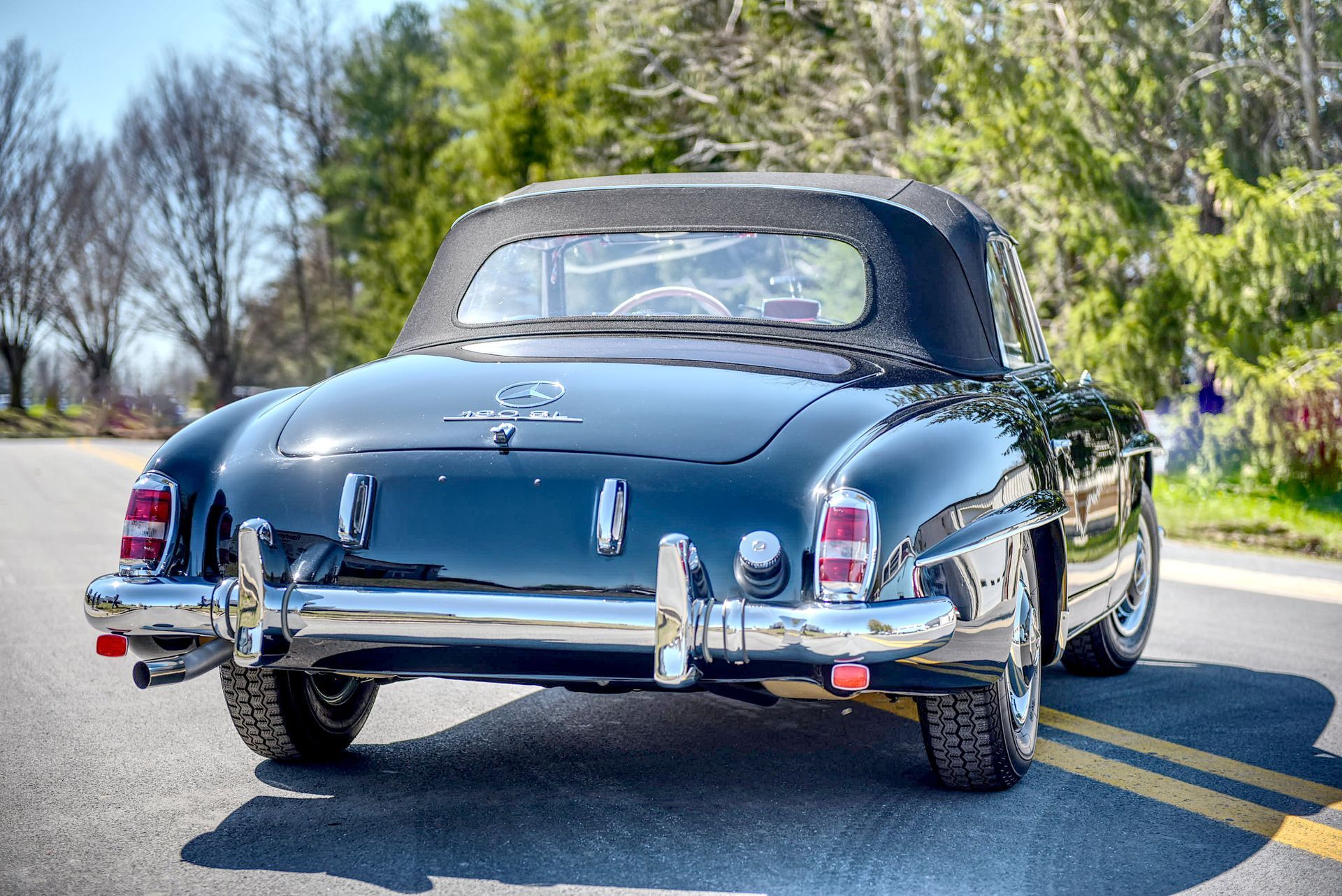 Black Mercedes-Benz 190SL convertible parked on a road, soft top up.