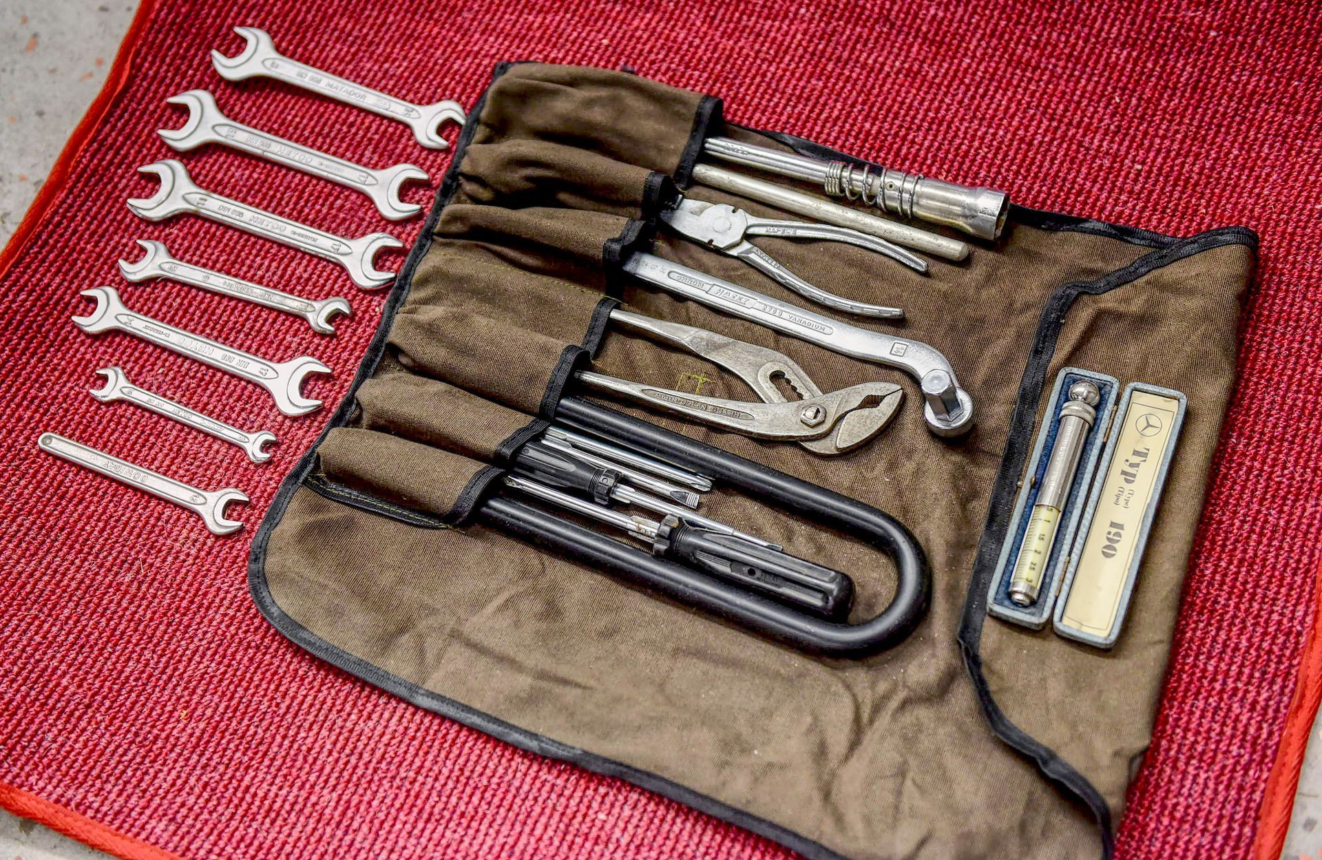Tool kit with various wrenches, pliers, and other tools, displayed on a red surface.