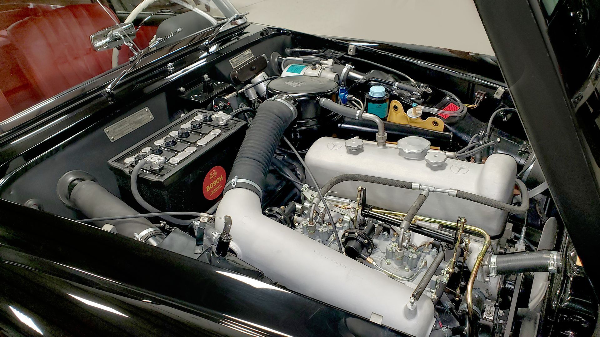 Black car engine bay with silver engine, black intake tube, and battery.