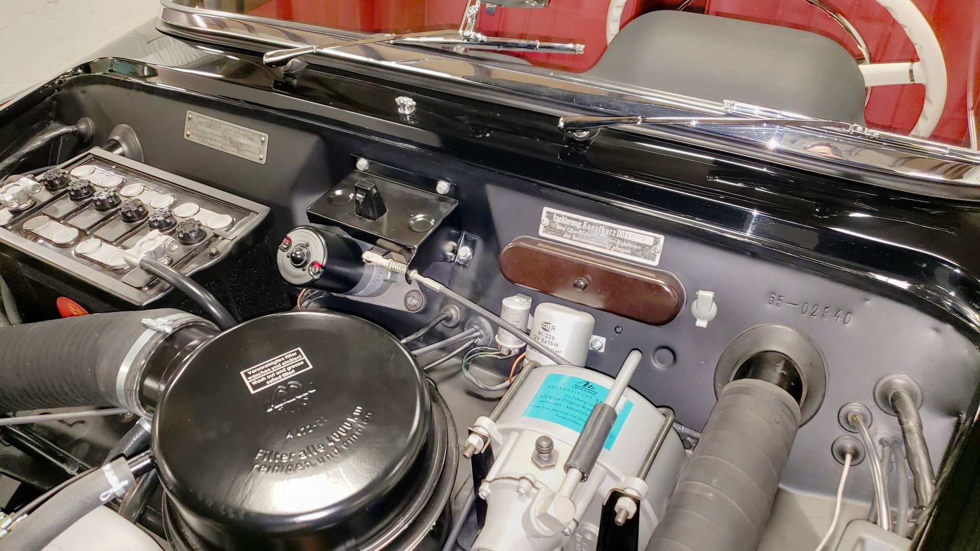 Engine compartment of a vintage black car, showing various components like air filter, battery, and wiring.