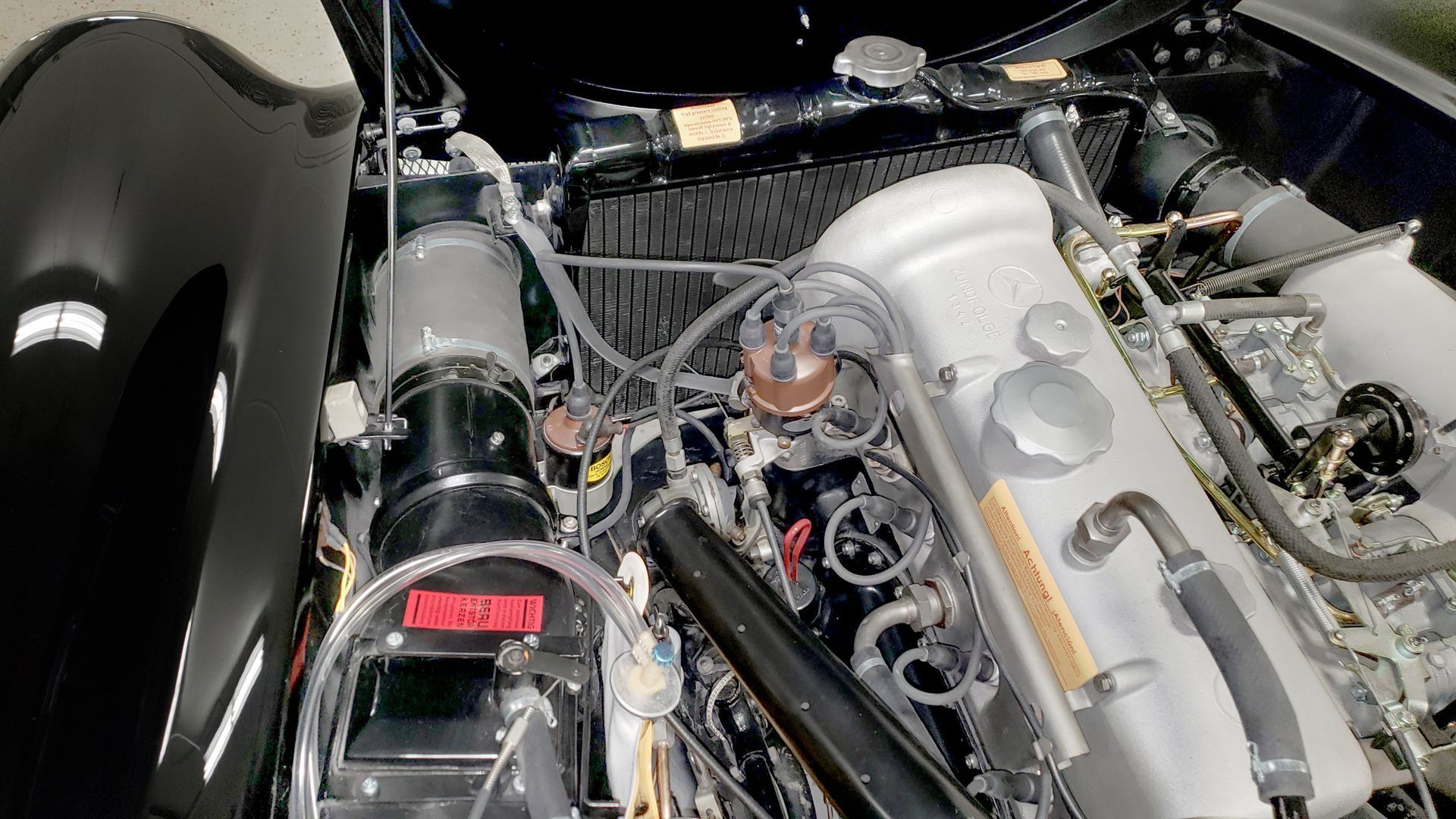 Black car engine compartment, various parts and hoses visible.
