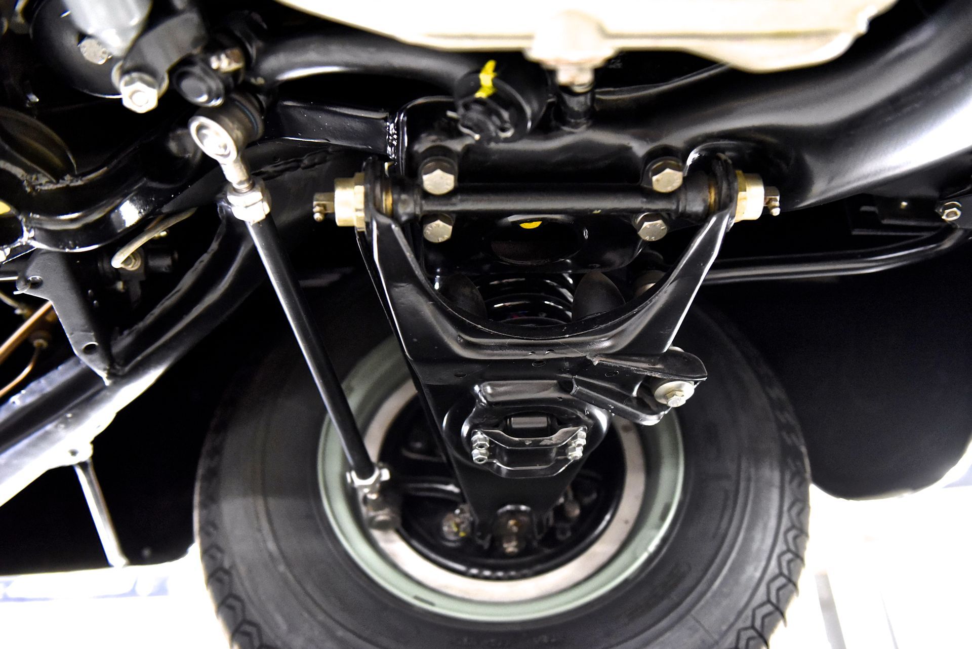 Black car suspension and tire, visible from beneath, with various metal components and bolts.