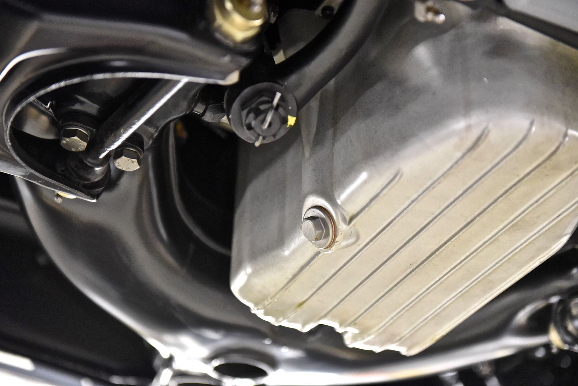 Underside of a car engine showing the oil pan, drain plug, and surrounding components.
