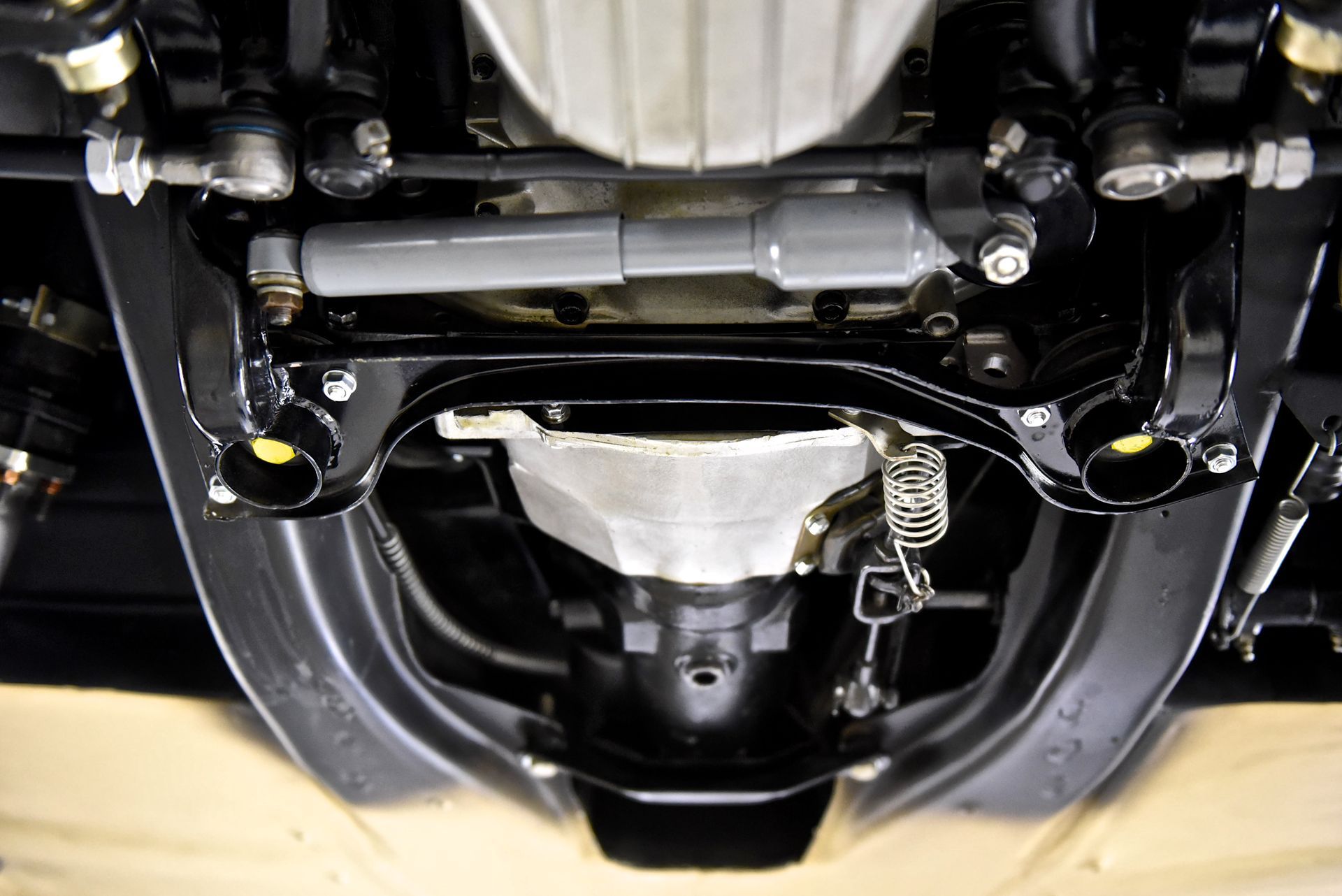 Undercarriage of a classic car showing steering components, suspension, and transmission in black and gray.