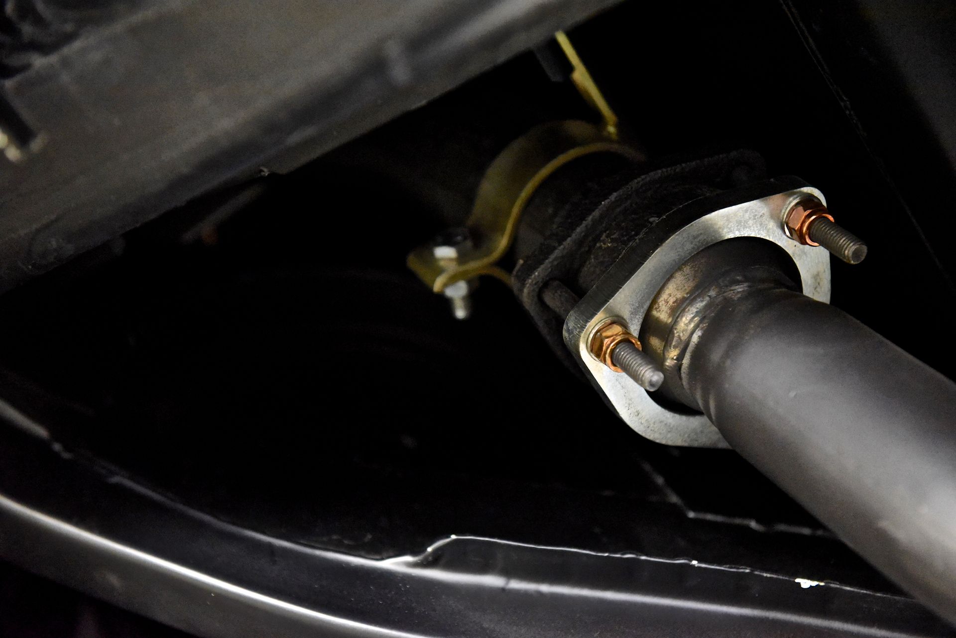 Exhaust pipe connection under a vehicle; metal flange, bolts, and clamp visible.