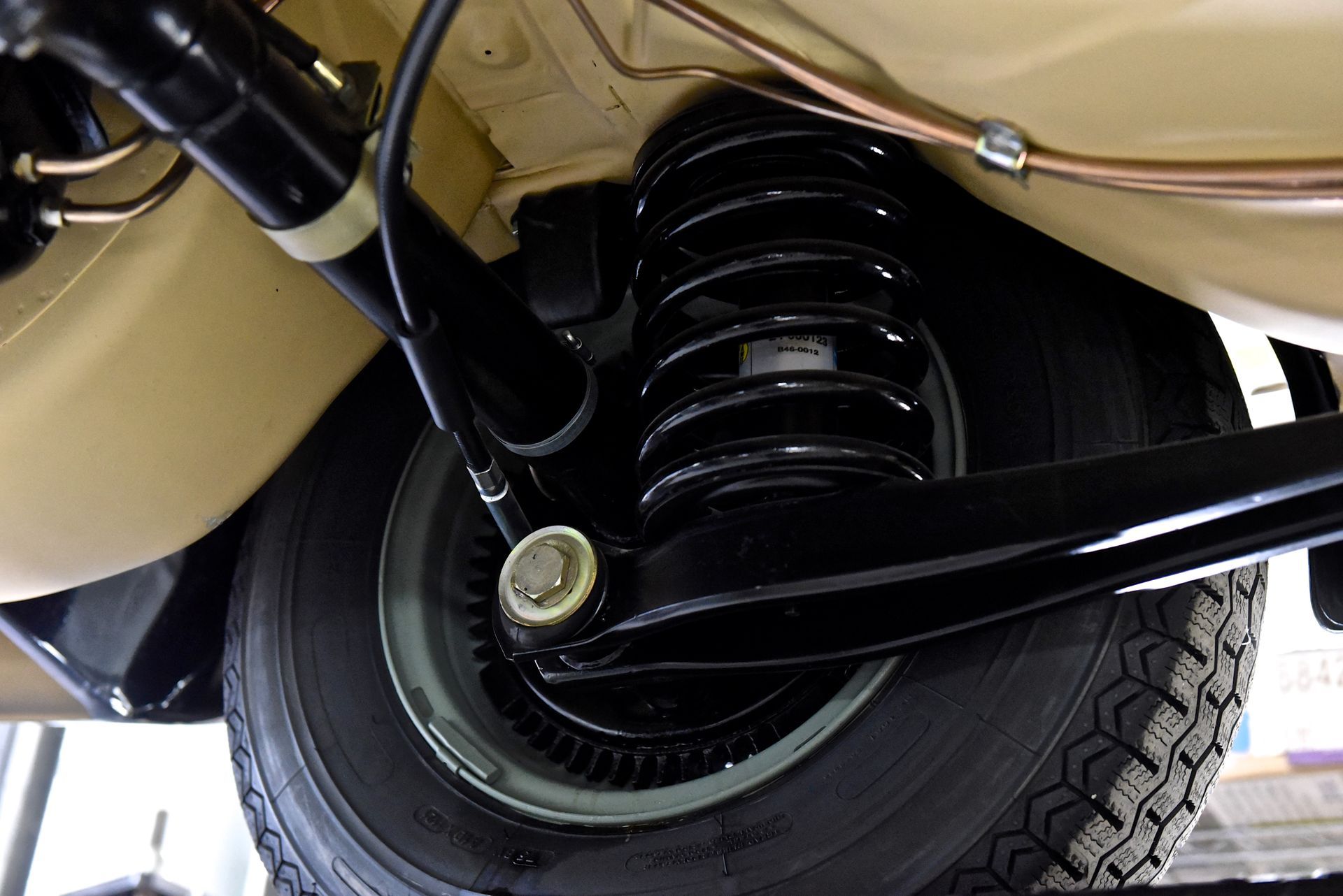 Black suspension and tire of a beige classic car, underside view.