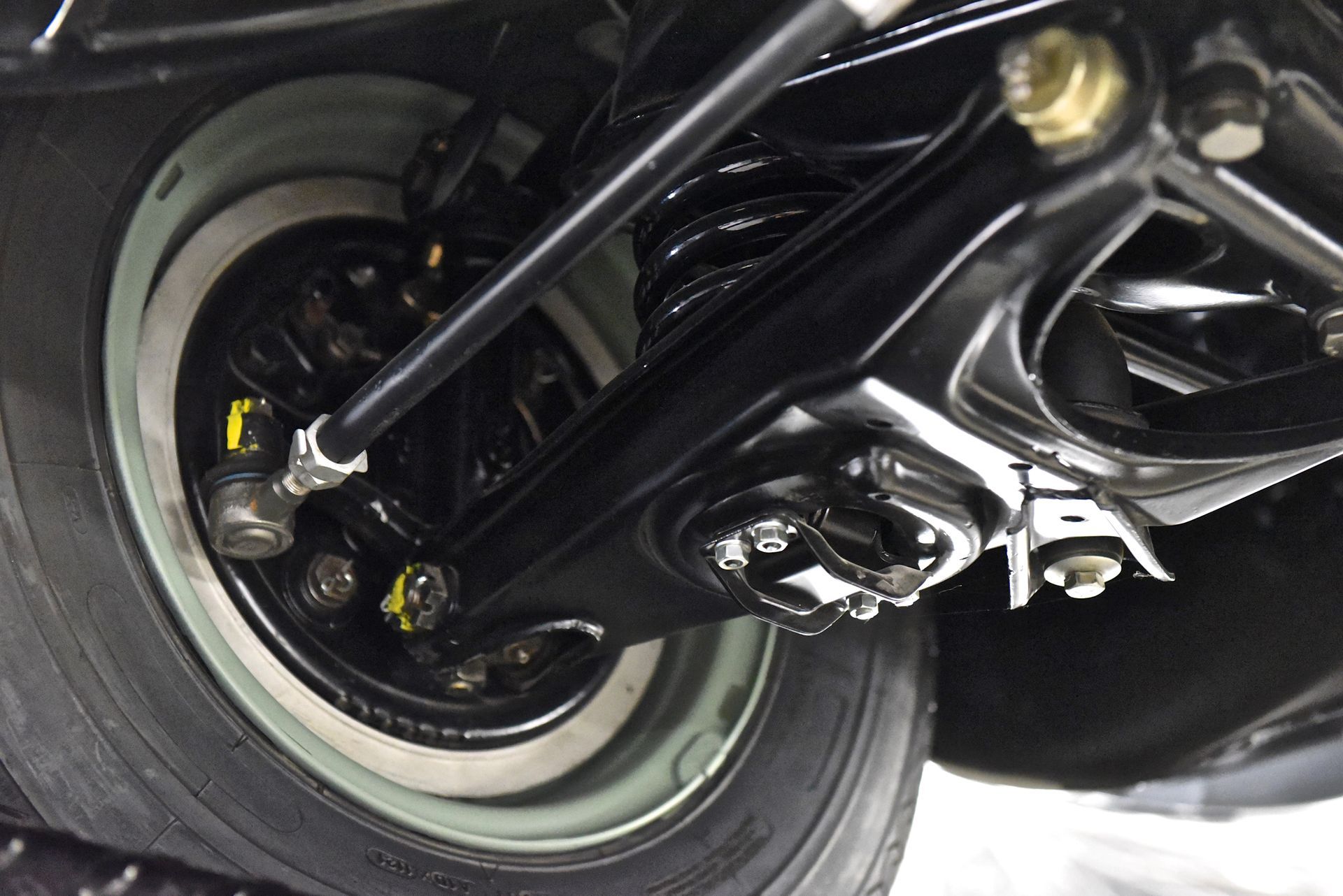 Black car suspension, tire, and wheel assembly. Whitewall tire against black components.